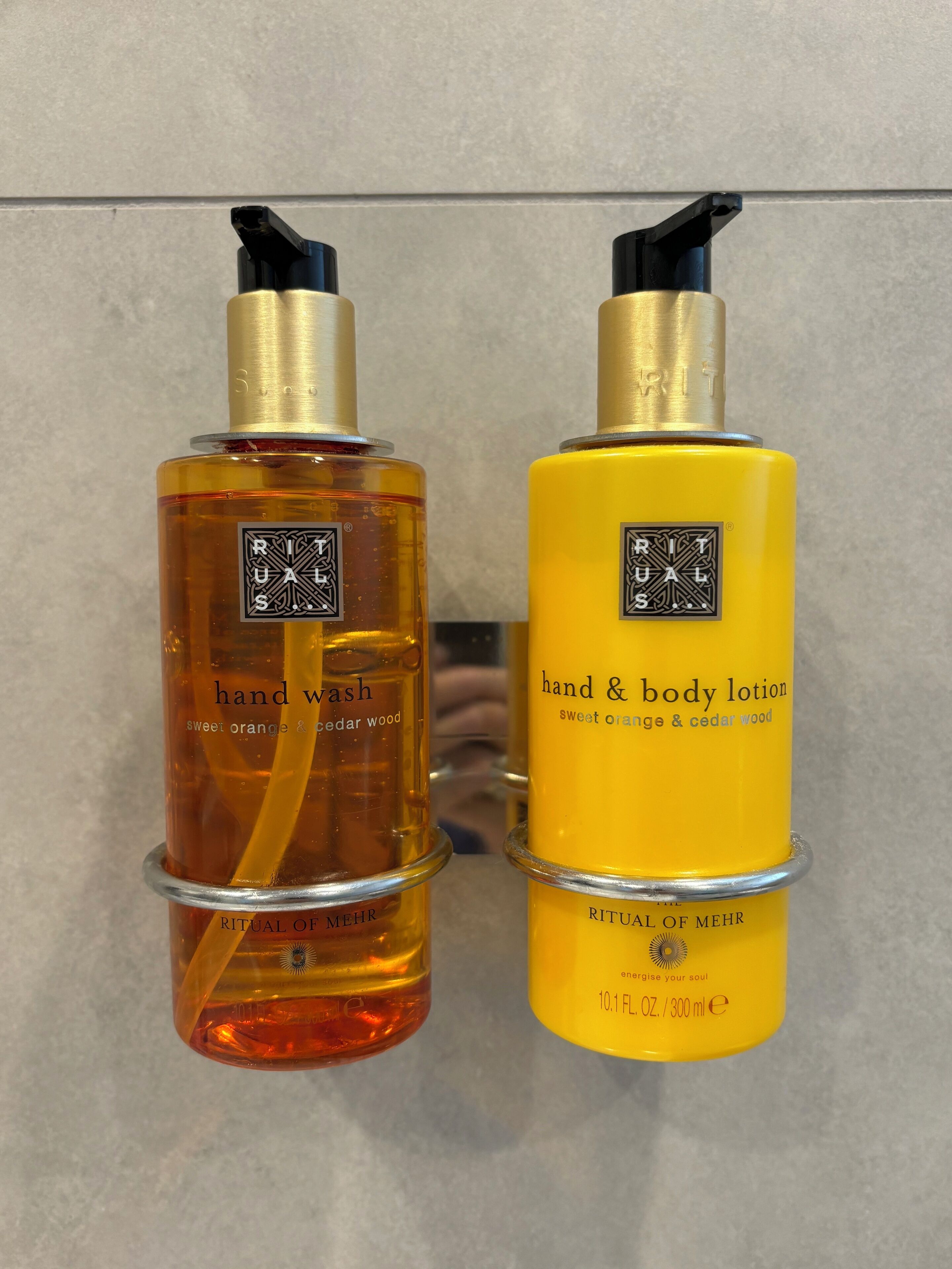 Deux flacons de savon pour les mains et de lotion pour le corps de la gamme Ritual of Mehr, chacun doté d’un distributeur à pompe et portant une étiquette indiquant le nom du produit et son parfum.
