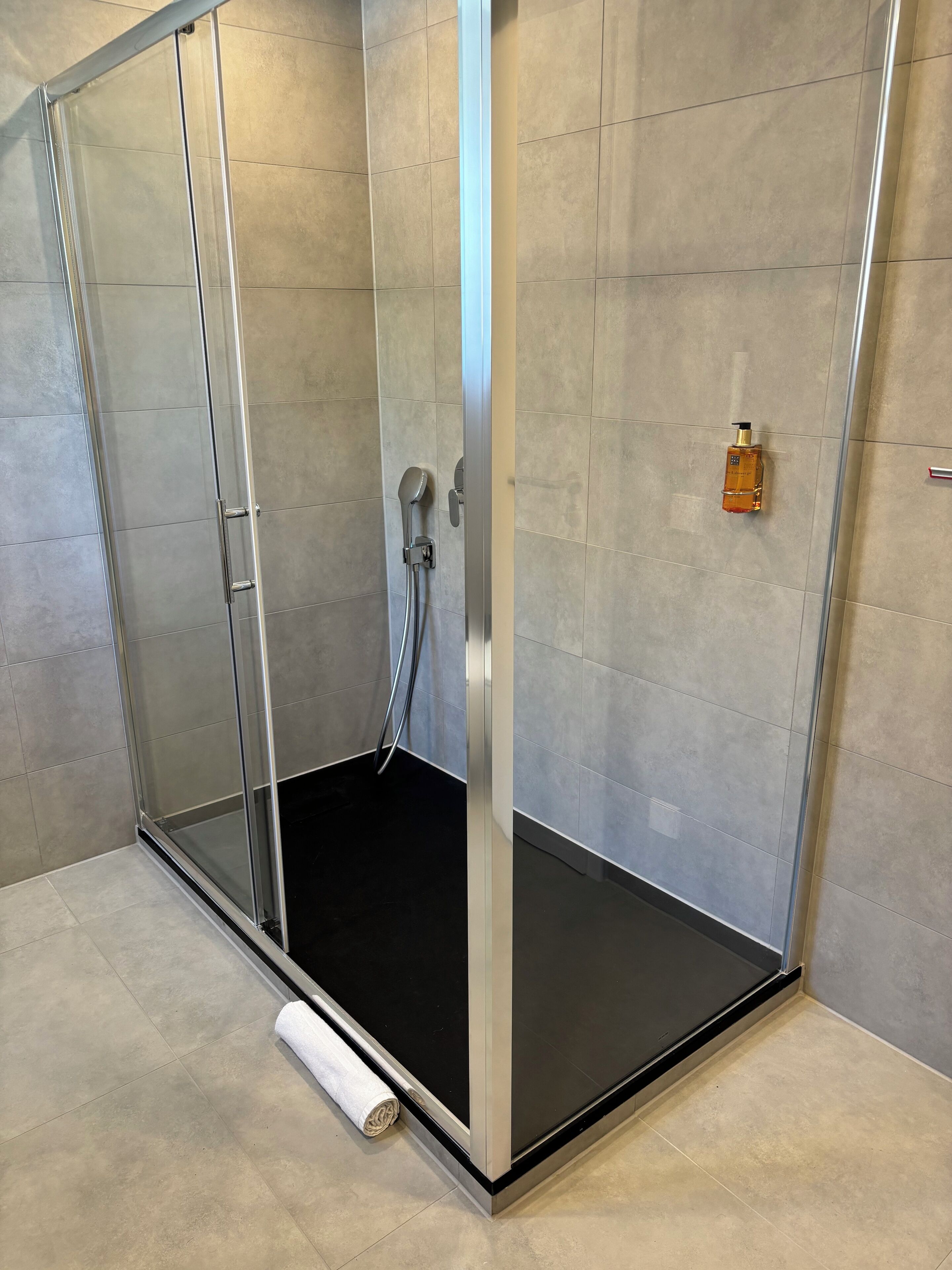 A modern shower enclosure with a glass door, a black floor, and a towel on the floor.
