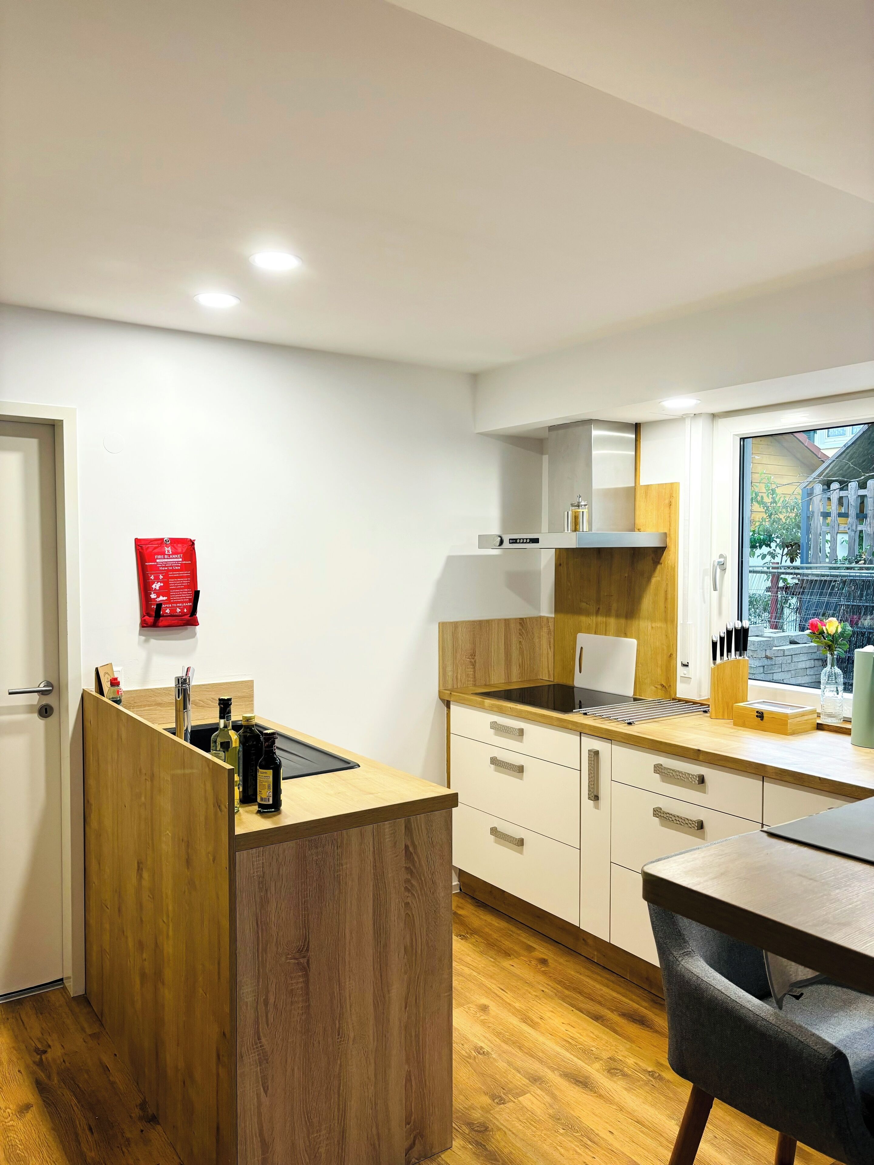 A modern kitchen with wooden cabinetry, a built-in stove, and a window with a view of the street.