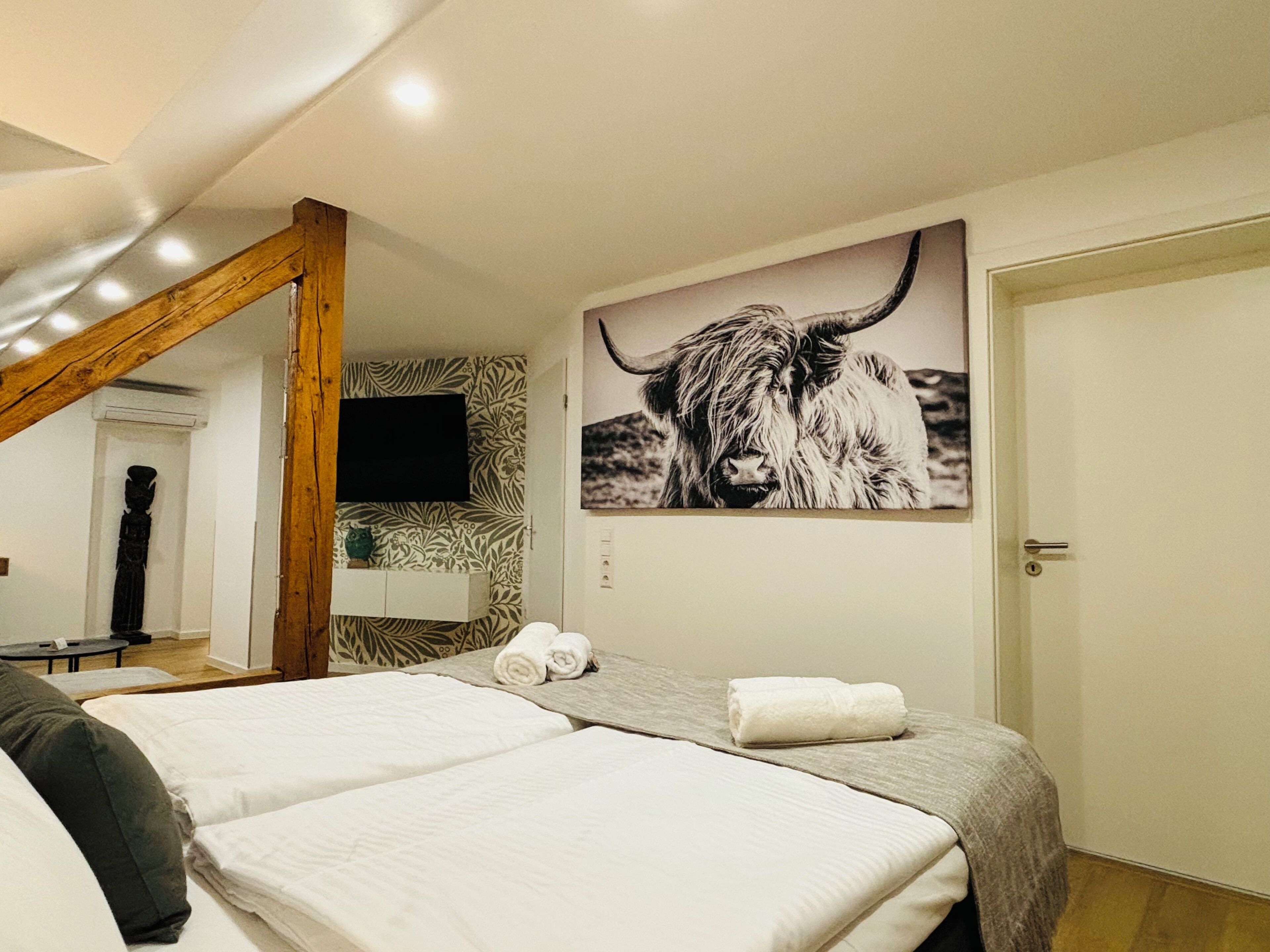 A hotel room with a large bed, a mounted artwork of a yak, and a wooden ceiling beam.