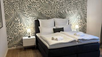 Een slaapkamer met een bed, nachtkastjes, een lamp, behang met een patroon en een geweven vloerkleed.