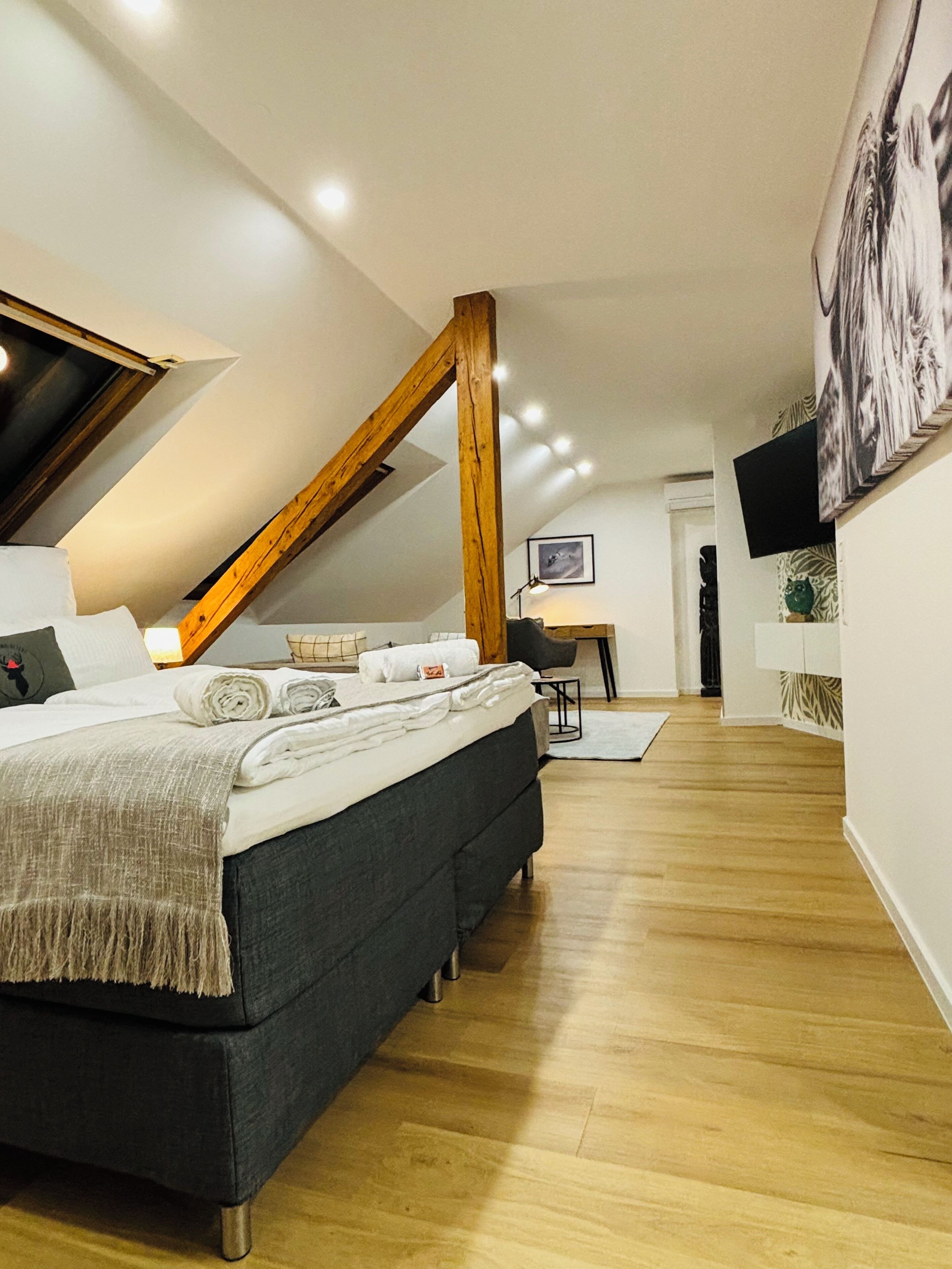 A modern bedroom with a loft-style ceiling, a bed with a dark headboard, and a desk area with a chair.