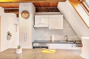 A kitchen with a clock, white cabinets, a stove, and a sink.