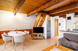 Un intérieur moderne comprenant un coin repas, un canapé, un téléviseur posé sur un meuble en bois, une cuisine et un escalier.