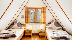 A triangular room with two beds, a window with curtains, a radiator, and a small table. - Holiday Home 'Twistesee 36' (Bad Arolsen)