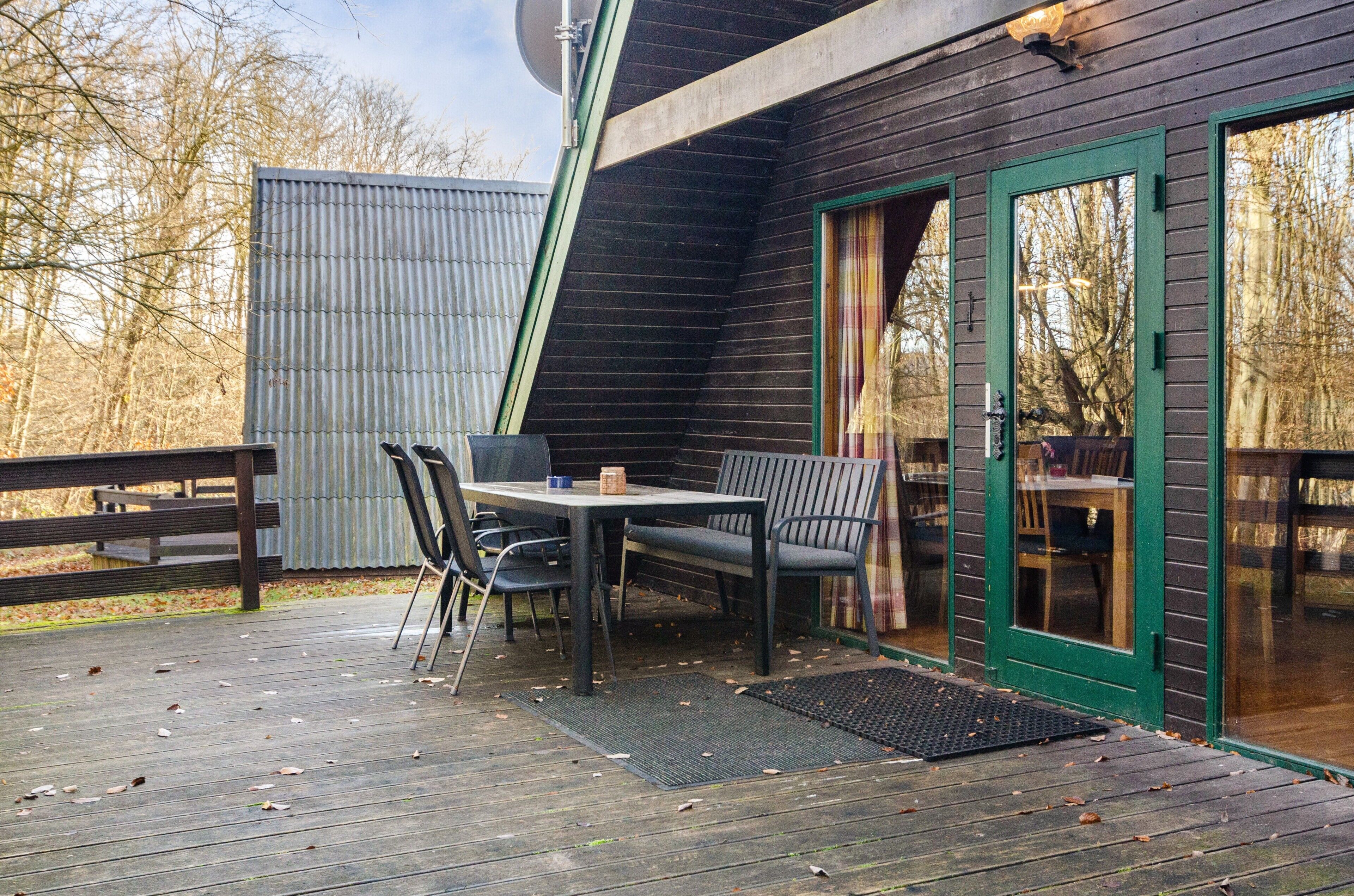 A wooden deck with a table and chairs, a green door, and a metal fence.