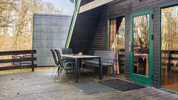 A wooden deck with a table and chairs, a green door, and a metal fence.