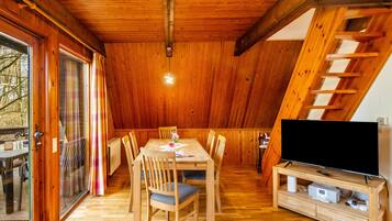 Ein Holzinterieur mit einem Esstisch, Stühlen, einem Fernseher auf einem Holzgestell und einem Fenster mit Vorhängen.