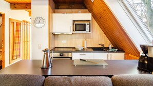A compact kitchen with a microwave, stove, and sink, a clock on the wall, and a window with a view of trees. - Holiday Home 'Twistesee 36' (Bad Arolsen)