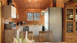 A wooden cabin interior with a kitchen, dining table, and a window.