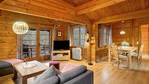 A wooden cabin interior with a sofa, dining table, chairs, a TV, and a fireplace.