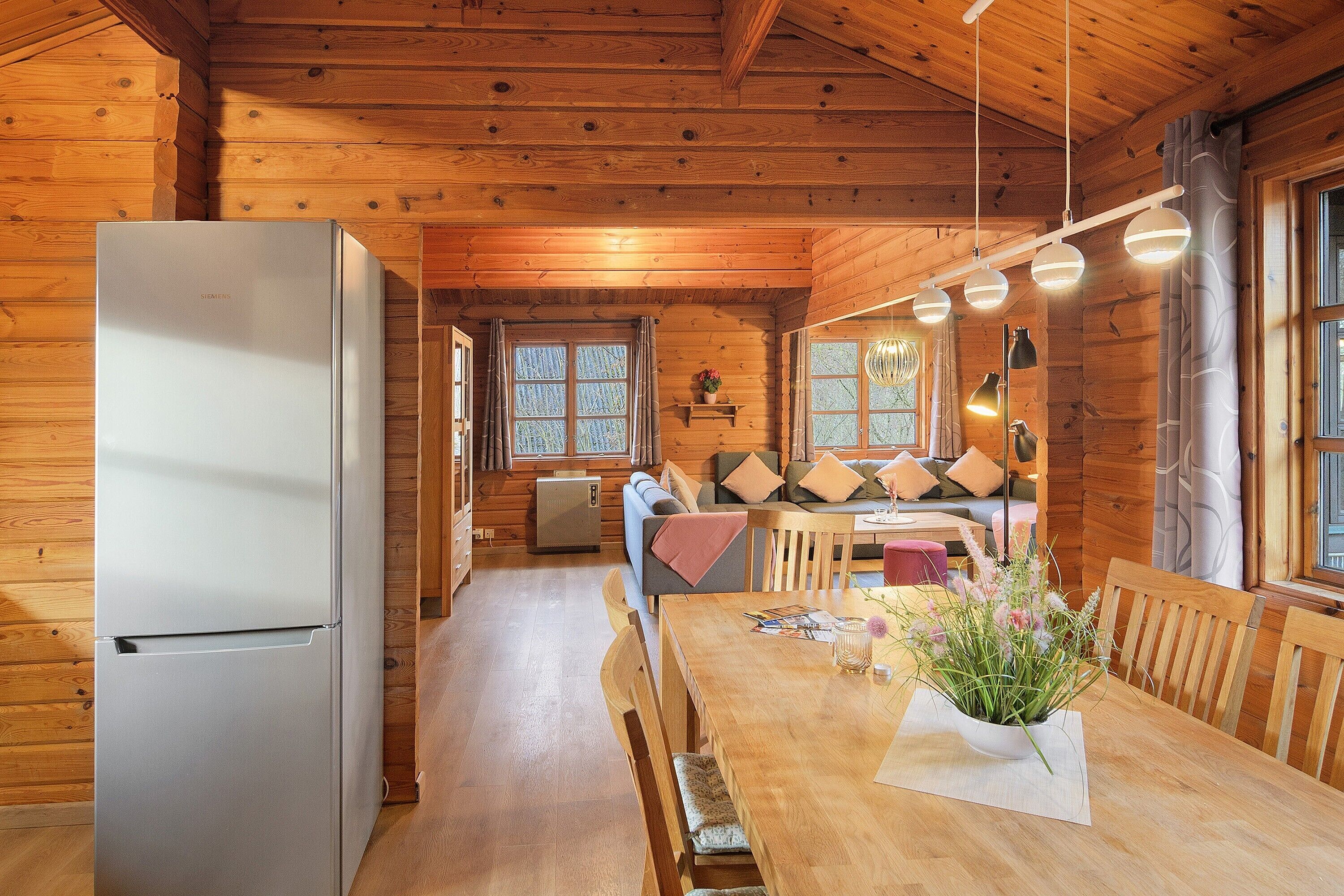 Interior de uma cabana de madeira, com geladeira, mesa de jantar e um sofá.