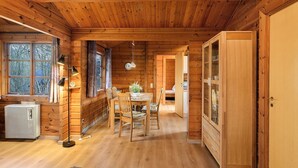 A wooden cabin interior with a dining table, chairs, a lamp, and a cabinet.
