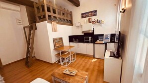 A compact living space with a kitchenette, a wooden ladder, a dining area with a table and chairs, and a small sofa. - Chez Giulia Cassis - Studio near the beach (Cassis)