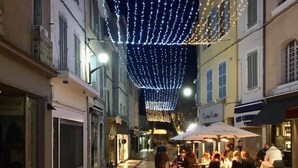 A street with buildings on either side, decorated with string lights. There are tables and chairs outside a building, suggesting a cafe or restaurant. - Chez Giulia Cassis - Studio near the beach (Cassis)
