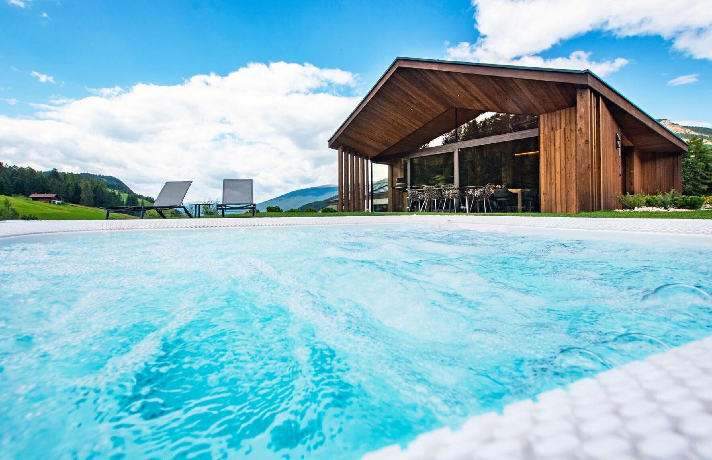 A swimming pool with lounge chairs and a wooden building with large windows.
