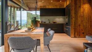 A modern kitchen with a large island, wooden ceiling, and a view of the outdoors.