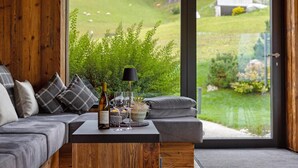 A modern interior with a wooden wall, grey sofa, and a table with a bottle, glasses, and a bowl.