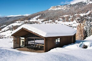 Une cabane en bois avec un toit enneigé, de grandes fenêtres et un espace patio.