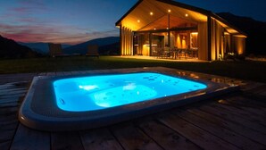 A hot tub on a wooden deck, a covered outdoor seating area, and a mountain backdrop.