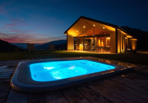 Un bain à remous sur une terrasse en bois, un espace salon extérieur abrité et une vue imprenable sur les montagnes.
