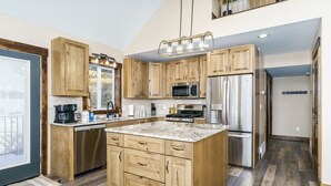 A modern kitchen with wooden cabinets, a central island, stainless steel appliances, and a large window. - Lava`s Red King of The Hill (Lava Hot Springs)