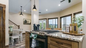 A kitchen with a central island, wooden cabinets, a stove, and a dining area with chairs. - Lava`s Red King of The Hill (Lava Hot Springs)