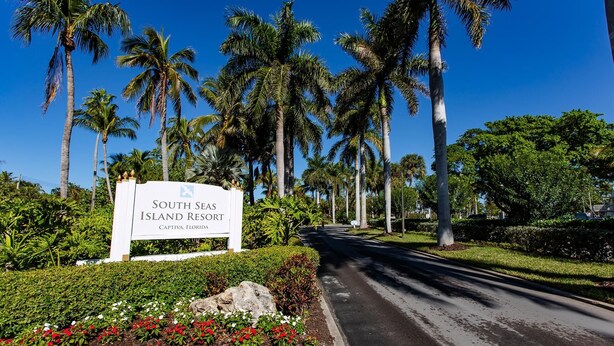A sign for South Seas Island Resort with a road leading through a palm tree-lined area.