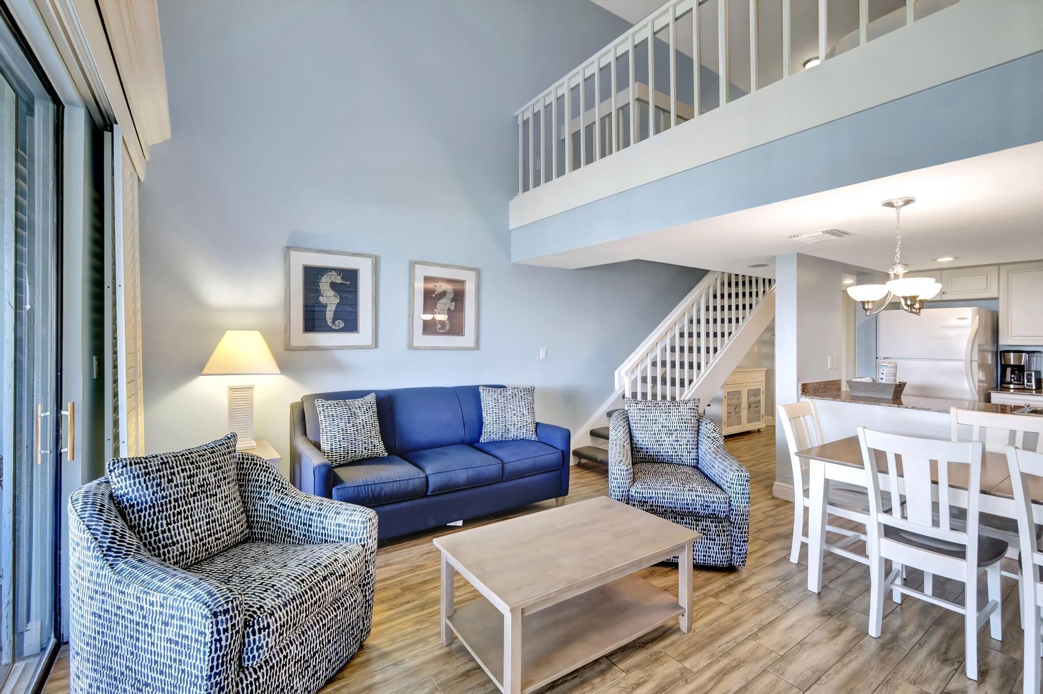 A living room with a blue sofa, patterned chairs, a wooden coffee table, and a staircase leading to an upper level.