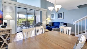 A dining area with a wooden table and chairs, a blue sofa, and a balcony with outdoor furniture.