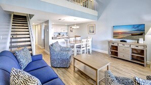 A spacious living area with a staircase, a dining table, and a kitchen in the background.