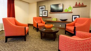 A hotel room with a seating area featuring orange patterned chairs, a coffee table, and a flat-screen TV mounted on the wall.