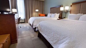 A hotel room with two beds, a desk with a TV, a chair, and a lamp.