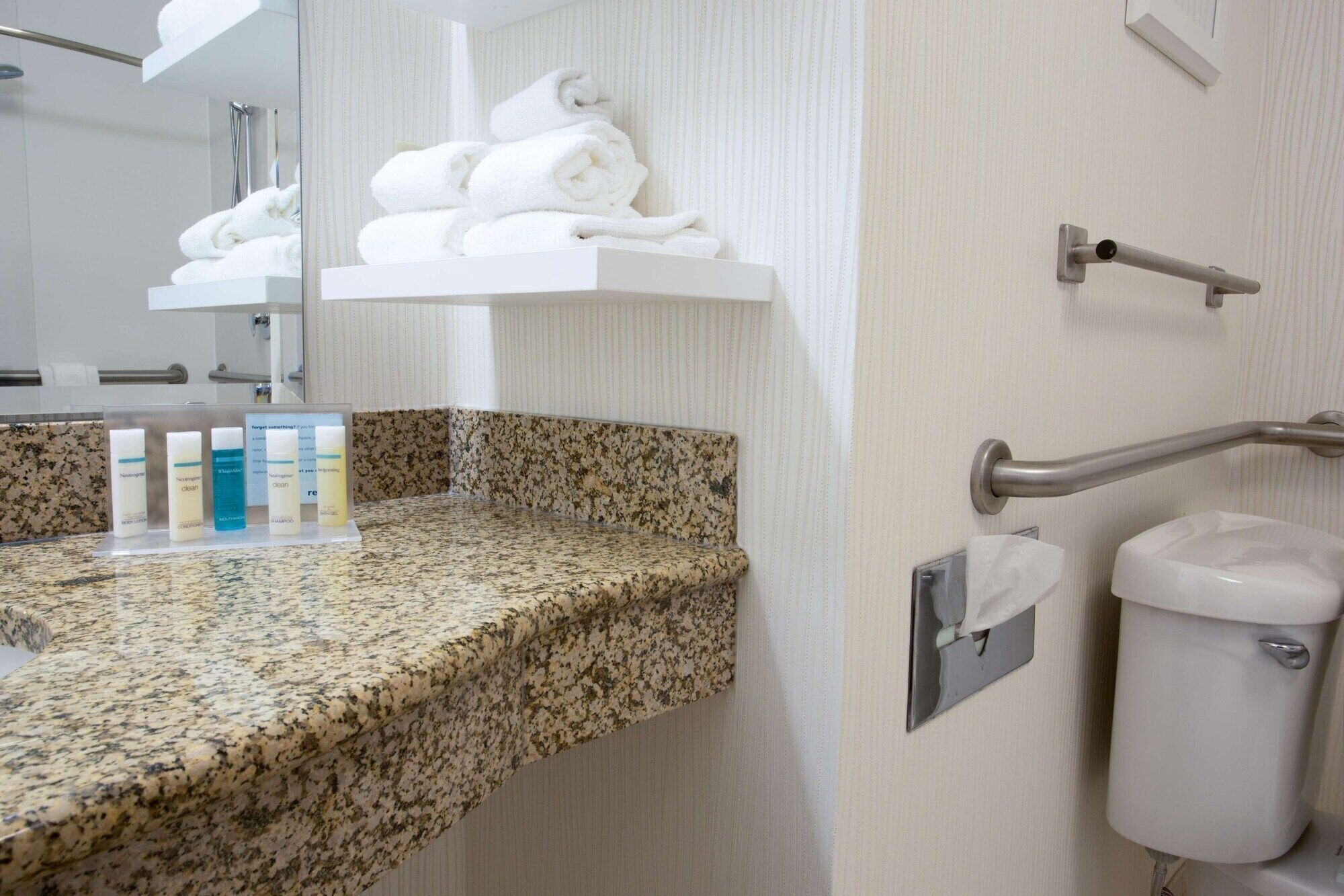 A bathroom with a granite countertop, a white sink, a towel rack with folded towels, and a hand dryer.