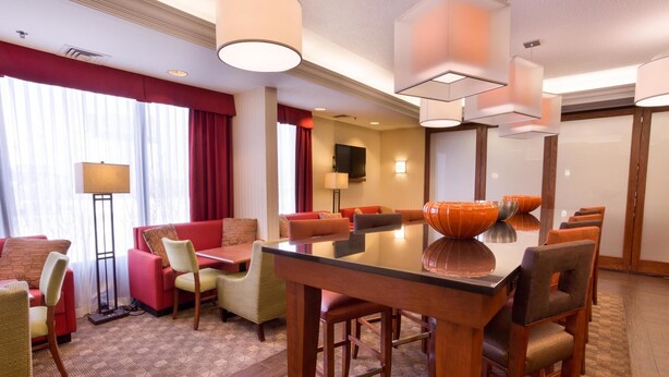 A hotel room with a dining area, a sofa set, a flat-screen TV, and a large window with curtains.
