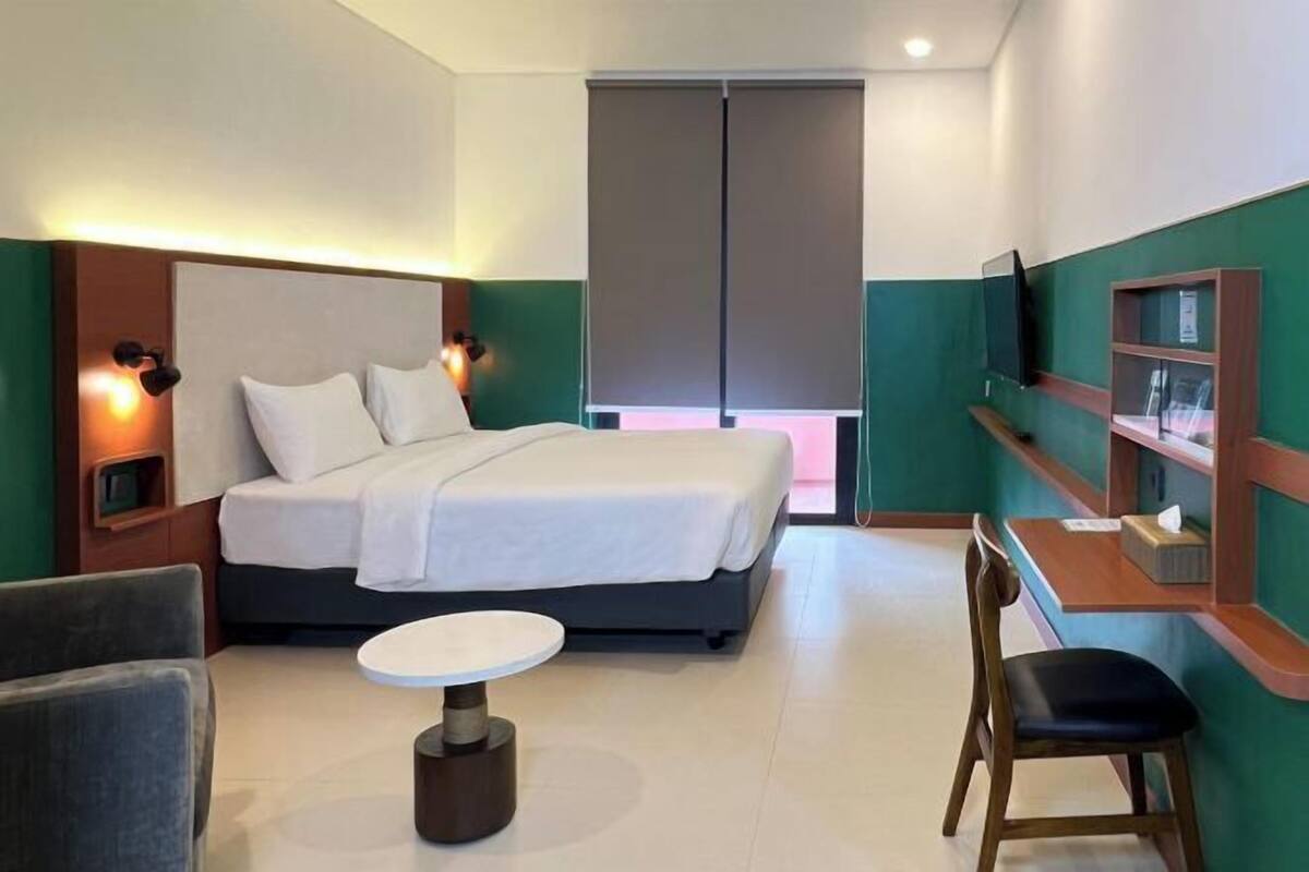 Une chambre d’hôtel avec un lit, une petite table ronde, une chaise, un téléviseur et une étagère avec quelques objets.