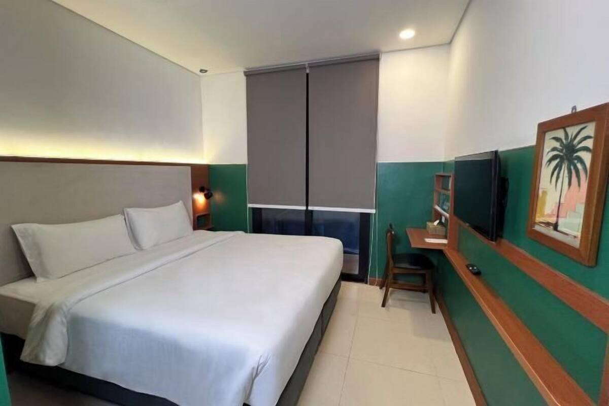 Une chambre d’hôtel équipée d’un lit, d’un bureau, d’une chaise, d’une télévision et d’une fenêtre avec des stores.