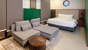 Et moderne hotelværelse med en hjørnesofa, en enkelt seng, et rundt vævet sofabord og en grøn accentvæg.