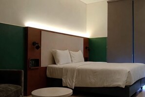 Quarto de hotel com cama, mesa redonda e cabeceira com iluminação embutida.