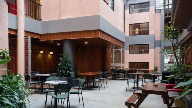 En udendørs café i flere etager med borde og stole, omgivet af planter og en murstensmur.
