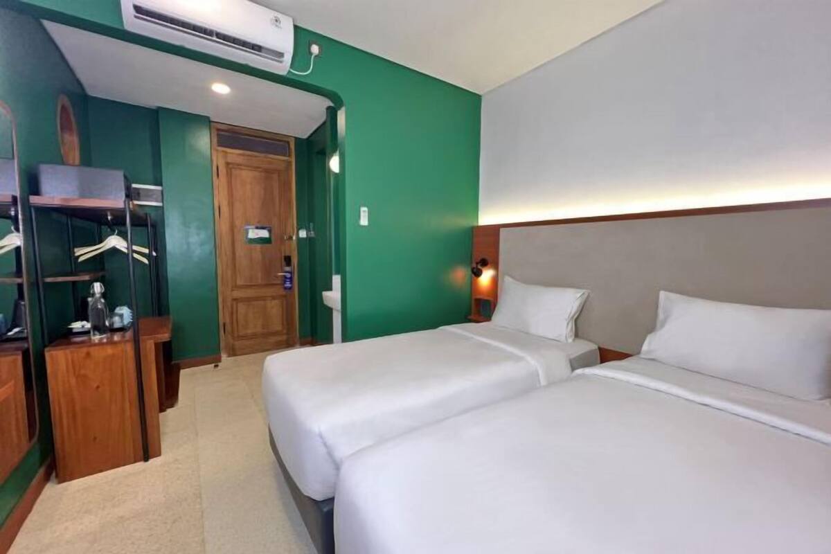 Une chambre d’hôtel avec deux lits, un bureau en bois, un miroir et un mur d’accent vert.