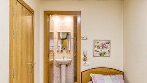 A bedroom with a wooden door, a bedside table, a bed with a quilt, a wall-mounted light fixture, and a framed floral artwork. - Bed and Breakfast 'Single Room 1' with Balcony, Wi-Fi and Air Conditioning (figueres)