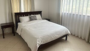 A neatly made bed with white bedding, a wooden headboard, and a small bedside table. - Spacious 4-bedroom villa with a Pool in serene Athiriver BAOB (Athi River)