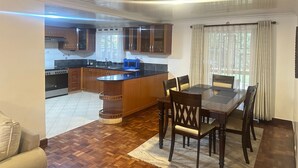 A modern kitchen with wooden cabinets, a central island, and a dining area with a table and chairs. - Spacious 4-bedroom villa with a Pool in serene Athiriver BAOB (Athi River)