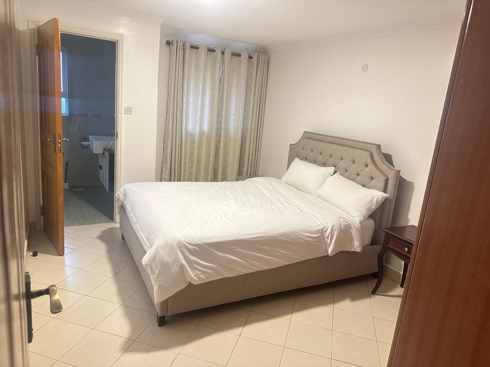 Een slaapkamer met een groot bed, een houten hoofdbord en een zichtbare badkamer door een open deur.