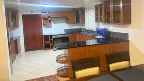 A kitchen with wooden cabinets, a stove, and a dining area with chairs. - Spacious 4-bedroom villa with a Pool in serene Athiriver BAOB (Athi River)