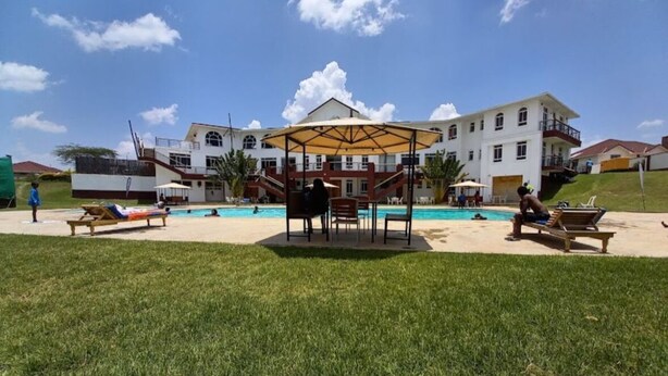 A pool area with lounge chairs and umbrellas, surrounded by a grassy lawn and a building with multiple windows and balconies. - Spacious 4-bedroom villa with a Pool in serene Athiriver BAOB (Athi River)