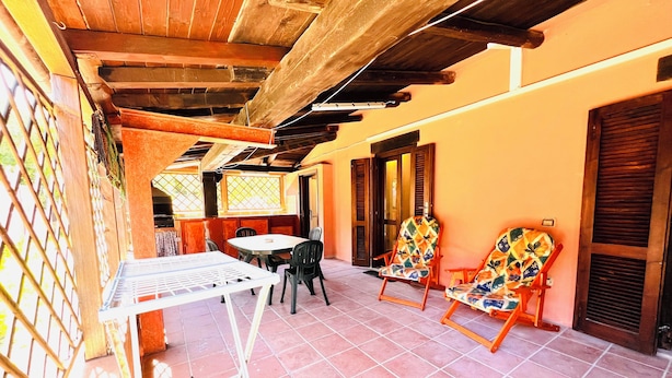 A covered patio area with a table and chairs, wooden beams, and a tiled floor. - Bilocale Lu Liciu H10 in Centro (San Teodoro)