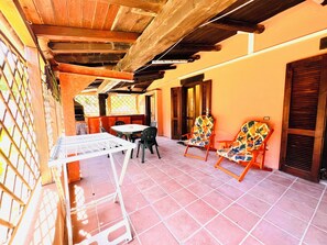 A covered patio area with a table and chairs, wooden beams, and a tiled floor. - Bilocale Lu Liciu H10 in Centro (San Teodoro)