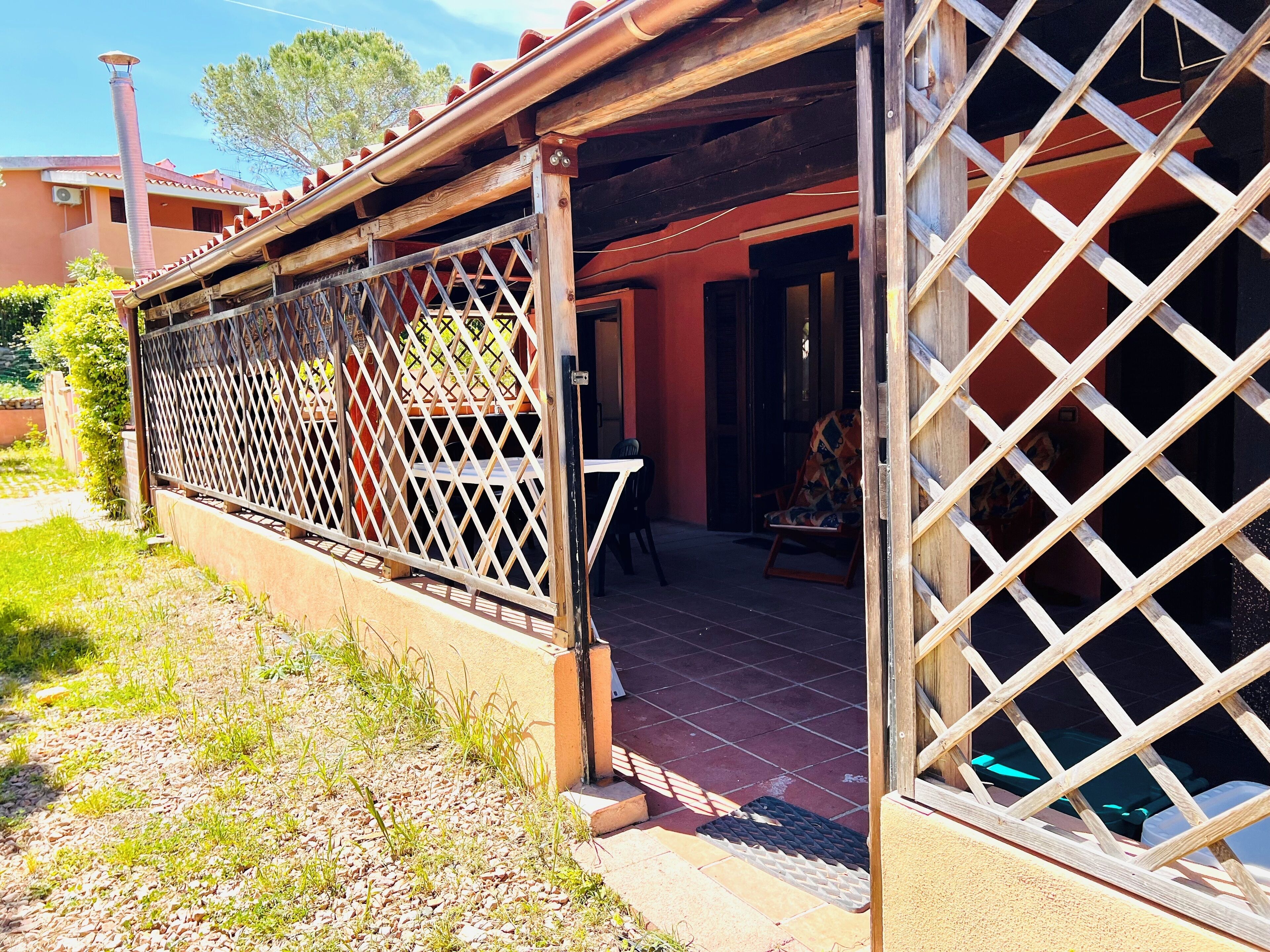 A covered outdoor area with a lattice fence, a door leading inside, and a chair outside.
